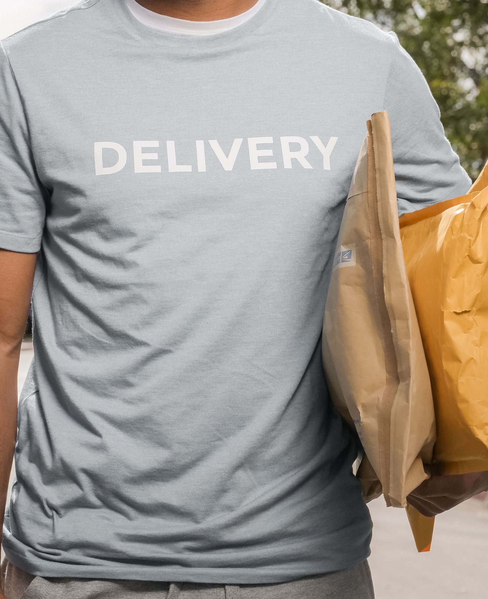 African American delivery man wearing a mask, holding parcels outside on a sunny day.