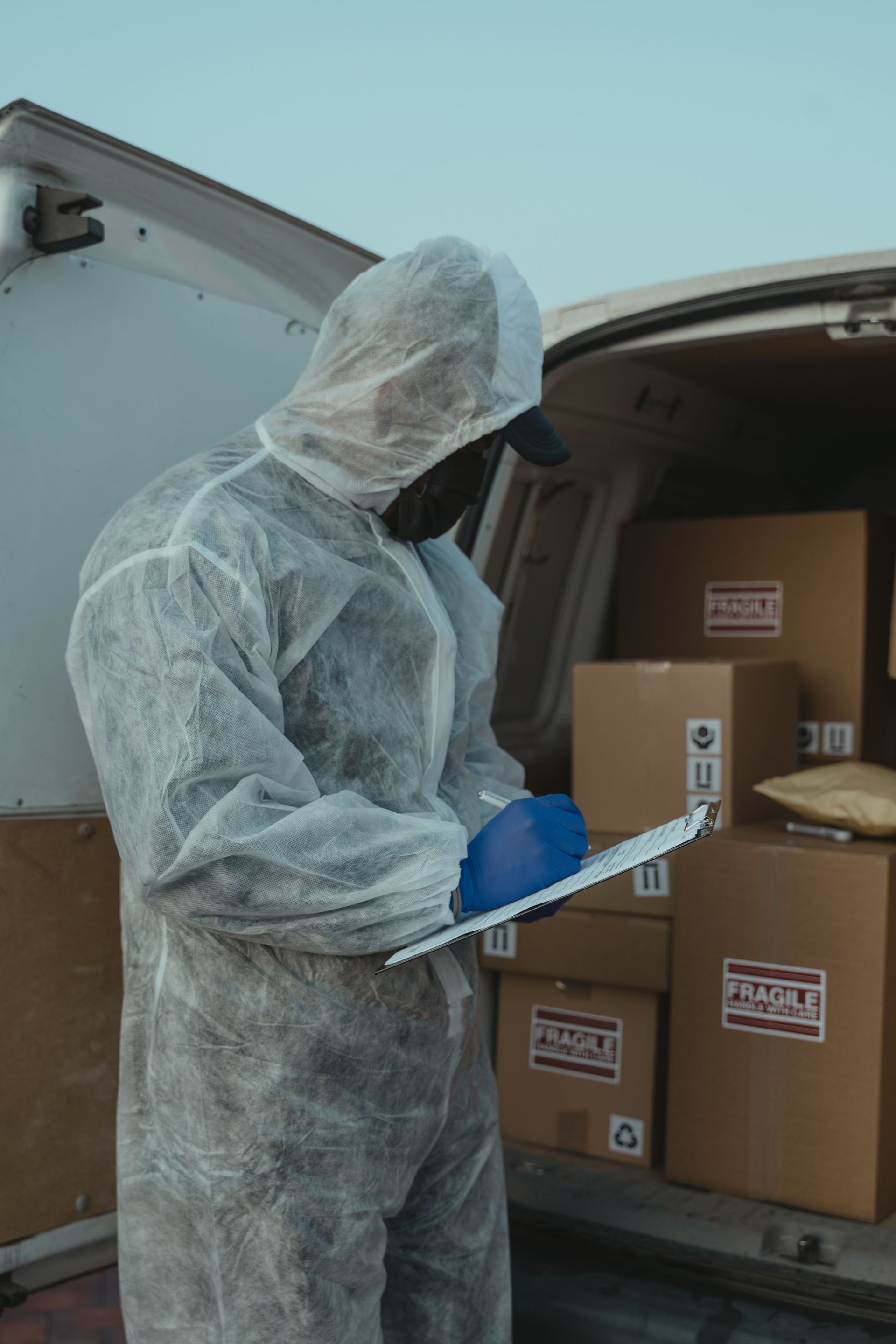 A logistics worker in PPE inspects packages in a delivery van for shipment.